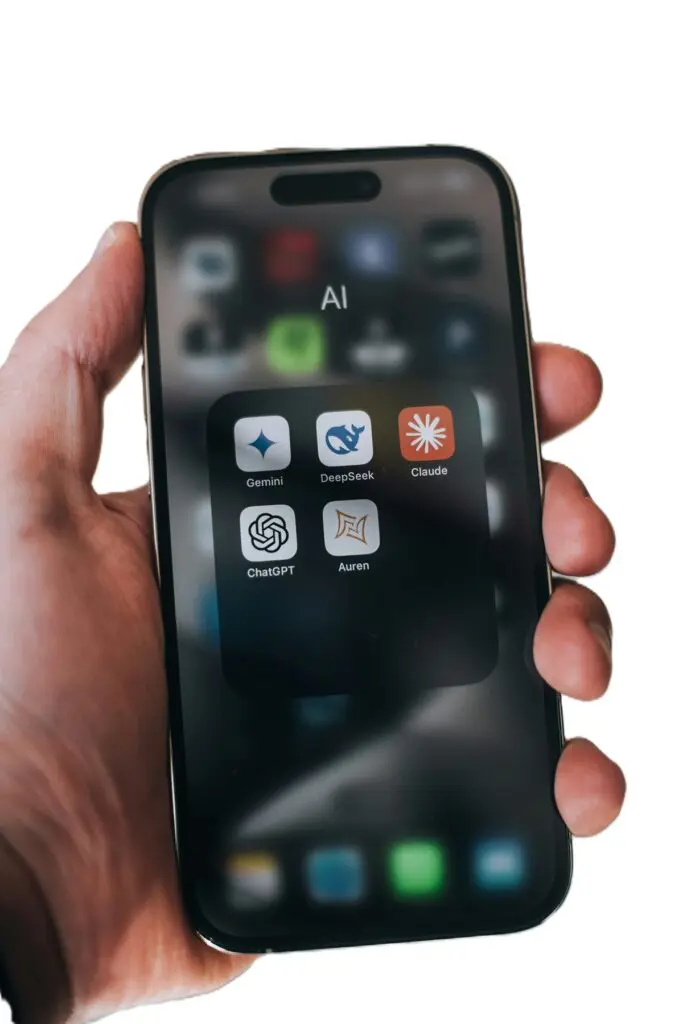 Hand holding a smartphone displaying an AI app folder with Gemini, DeepSeek, Claude, ChatGPT, and Auren icons on the screen.