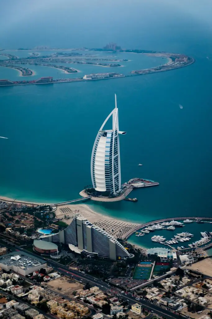 Aerial view of Dubai's Palm Jumeirah with the Burj Al Arab hotel in the foreground and turquoise sea surrounding the curved islands.