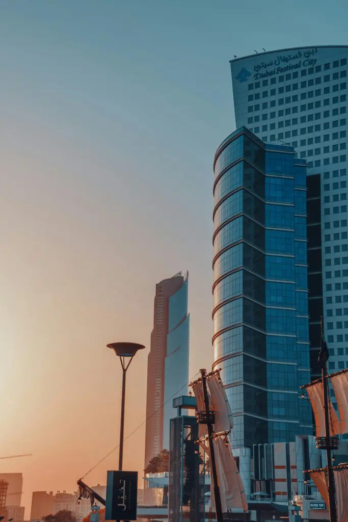 Tall modern skyscrapers at sunset, with a curved glass tower and a Dubai Festival City sign visible on the top of the building.